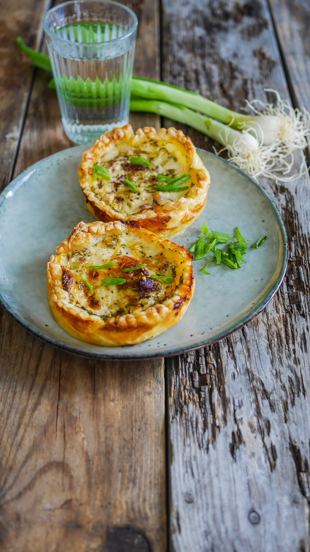 Tartelettes salées, oignons nouveaux, verre d'eau sur bois.