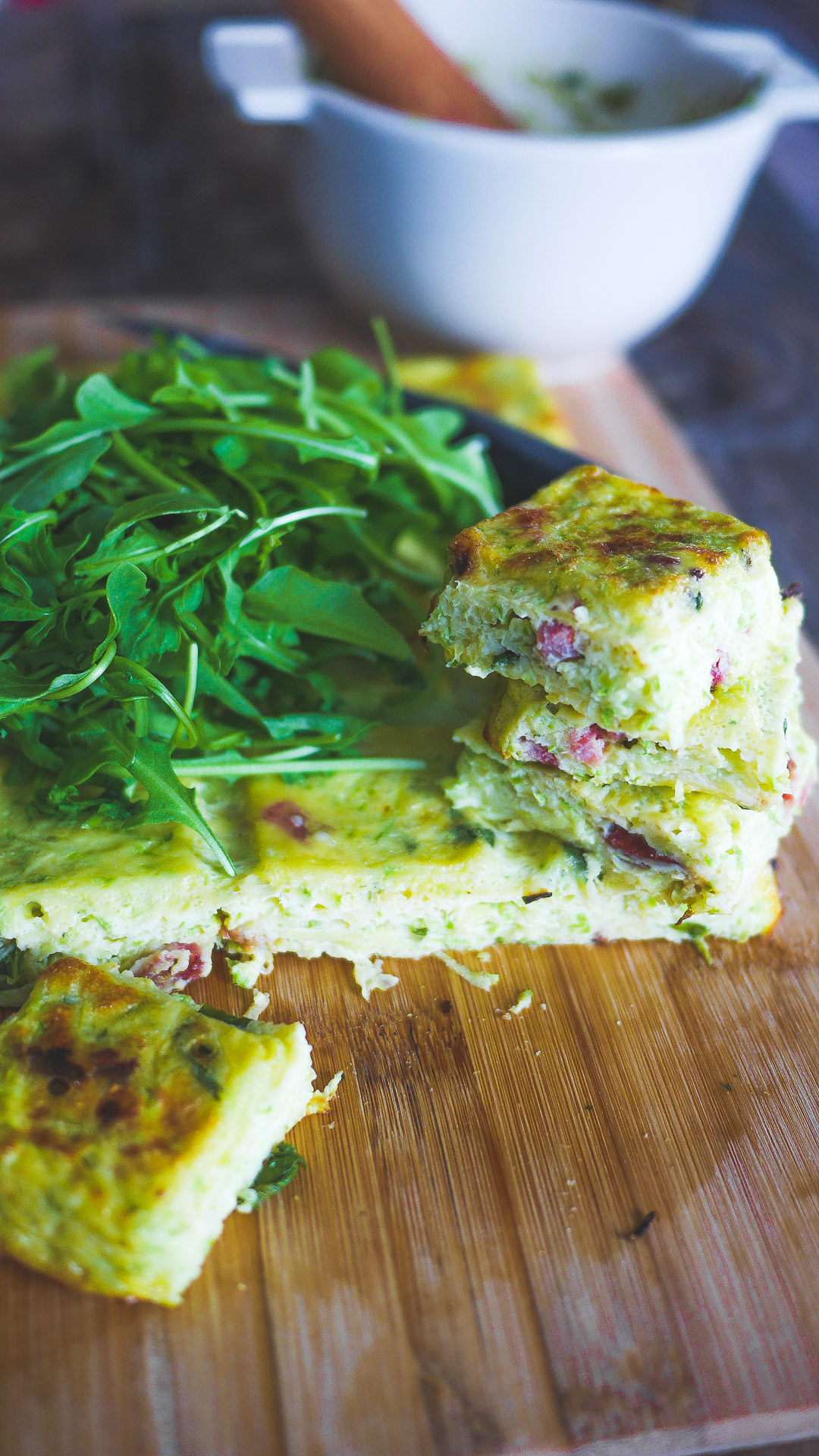Frittata coupée avec roquette, sur planche à découper en bois.
