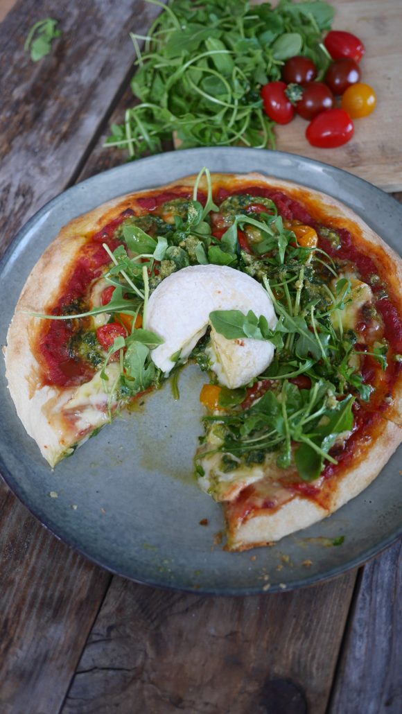 pizza au picodon roquette et pesto de basilic découpée dans une assiette