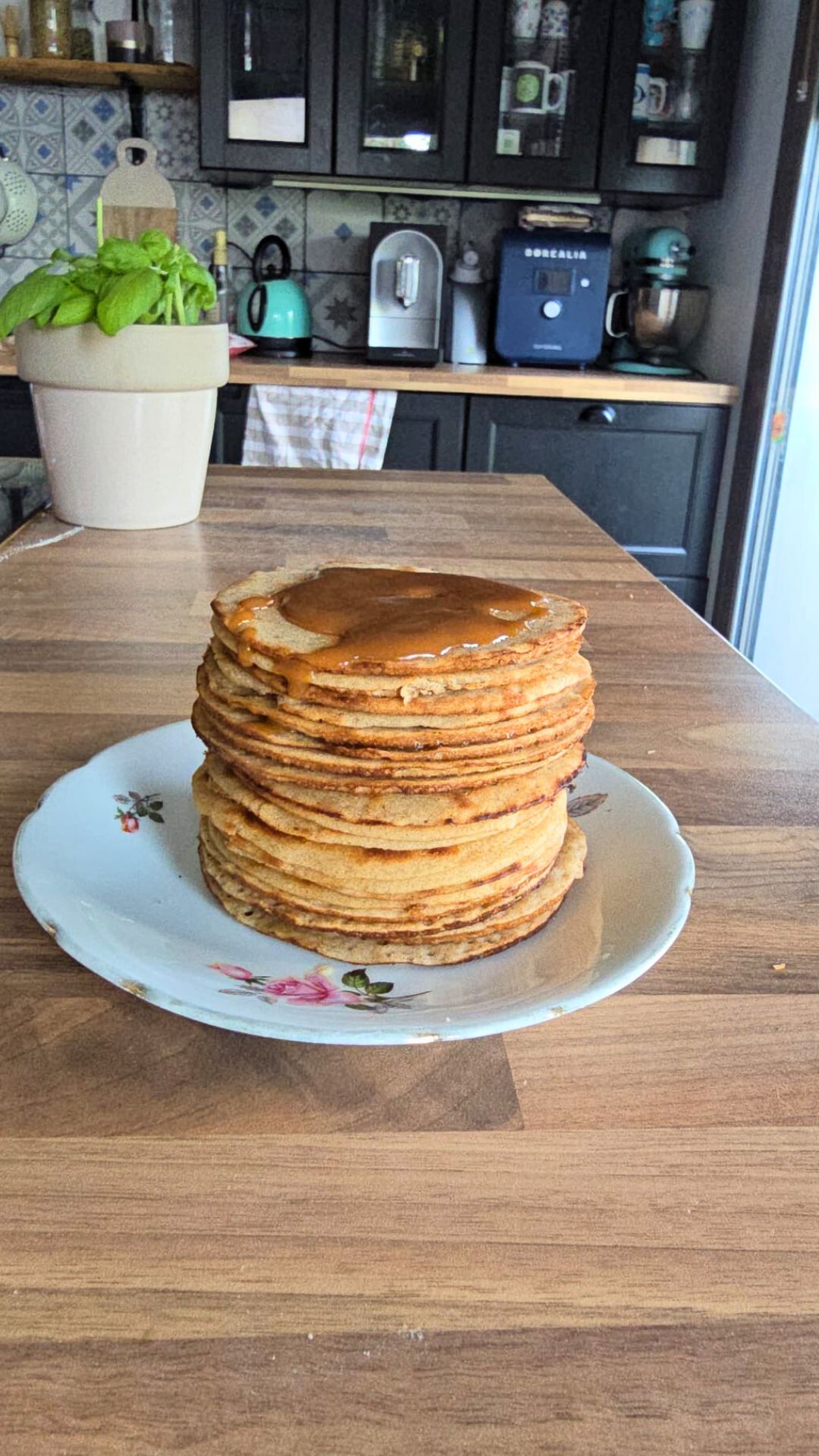 Pile de crêpes nappées de caramel sur une assiette fleurie.