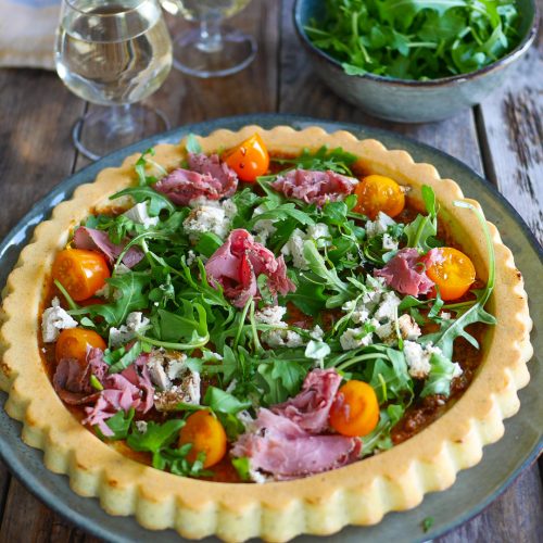 Tarte salée avec roquette, tomates, viande et fromage.