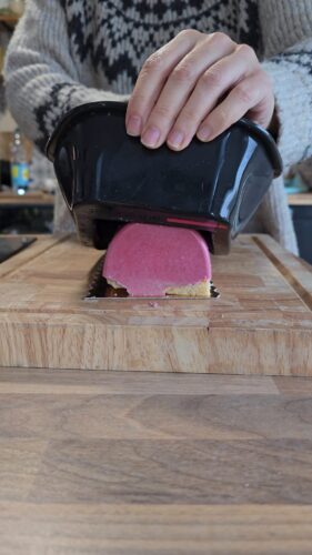 Personne coupant un gâteau rose avec un ustensile noir.