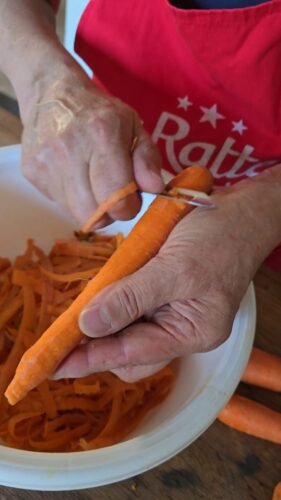 Préparation de carottes : épluchage avec un économe.