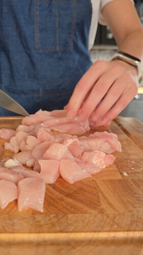 Personne coupant du poulet cru sur une planche à découper.