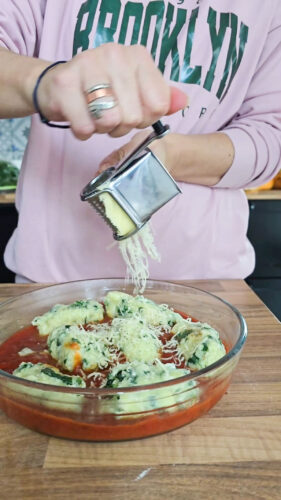 Râper du fromage sur des gnocchis aux épinards et sauce tomate.