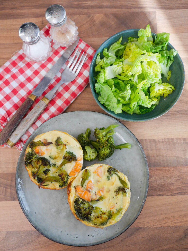 Quiches brocolis saumon posées sur une tables à manger avec salade verte et salière et poivrière