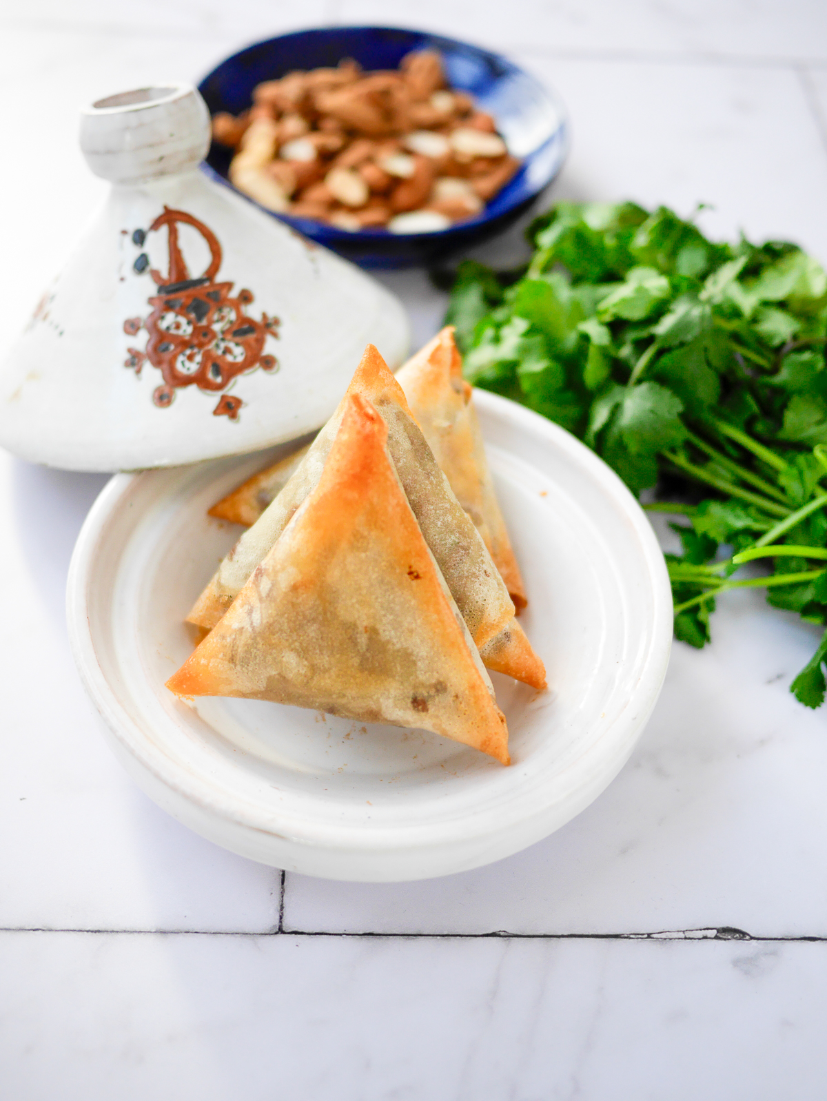 Briouats marocains, tajine et coriandre sur table blanche