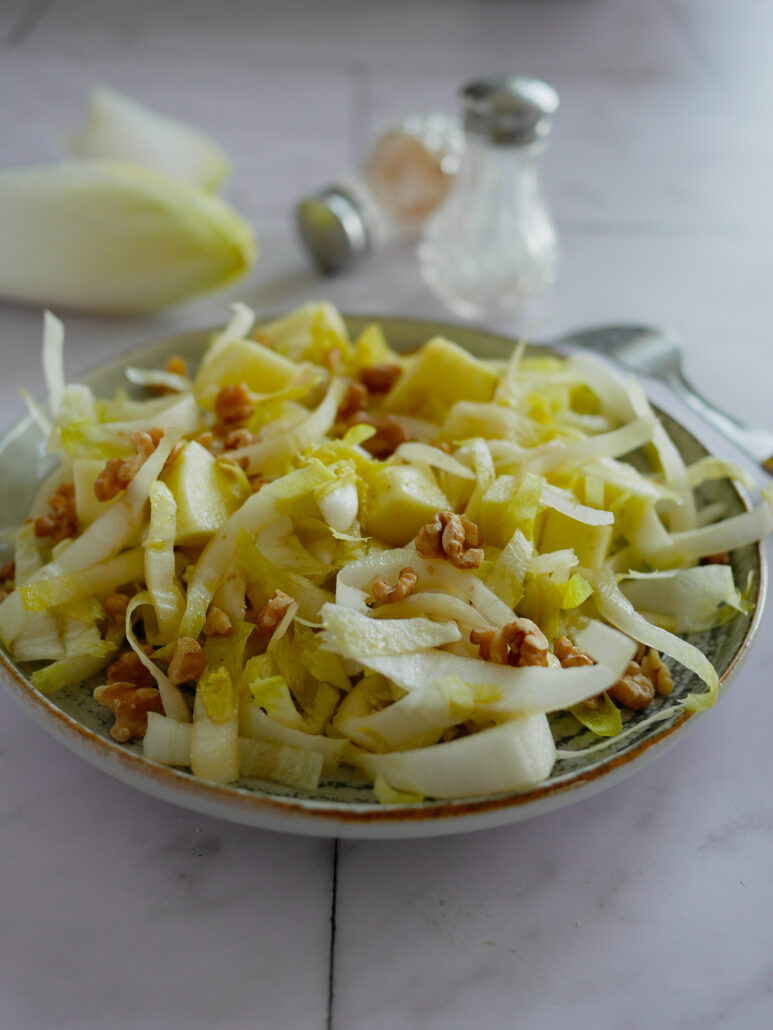 Assiette de salades d'endives avec des morceaux de pommes et des cerneaux de noix