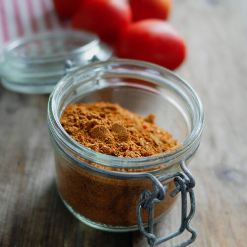 Épices dans un bocal avec tomates en arrière-plan.