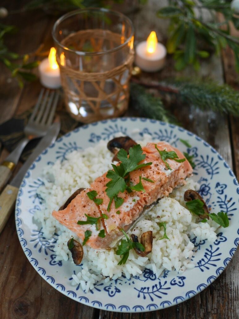 Assiette dressée avec un risotto crémeux aux champignons et huile de truffe, surmonté d'un pavé de saumon cuit à la vapeur et de persil frais.